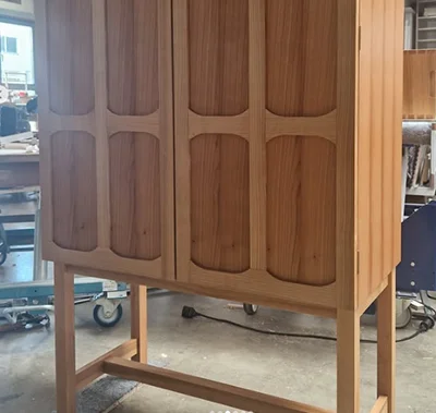 Massives Highboard aus Holz mit filigranen Beinen und markanten, organisch geformten Fräsungen in den Türen