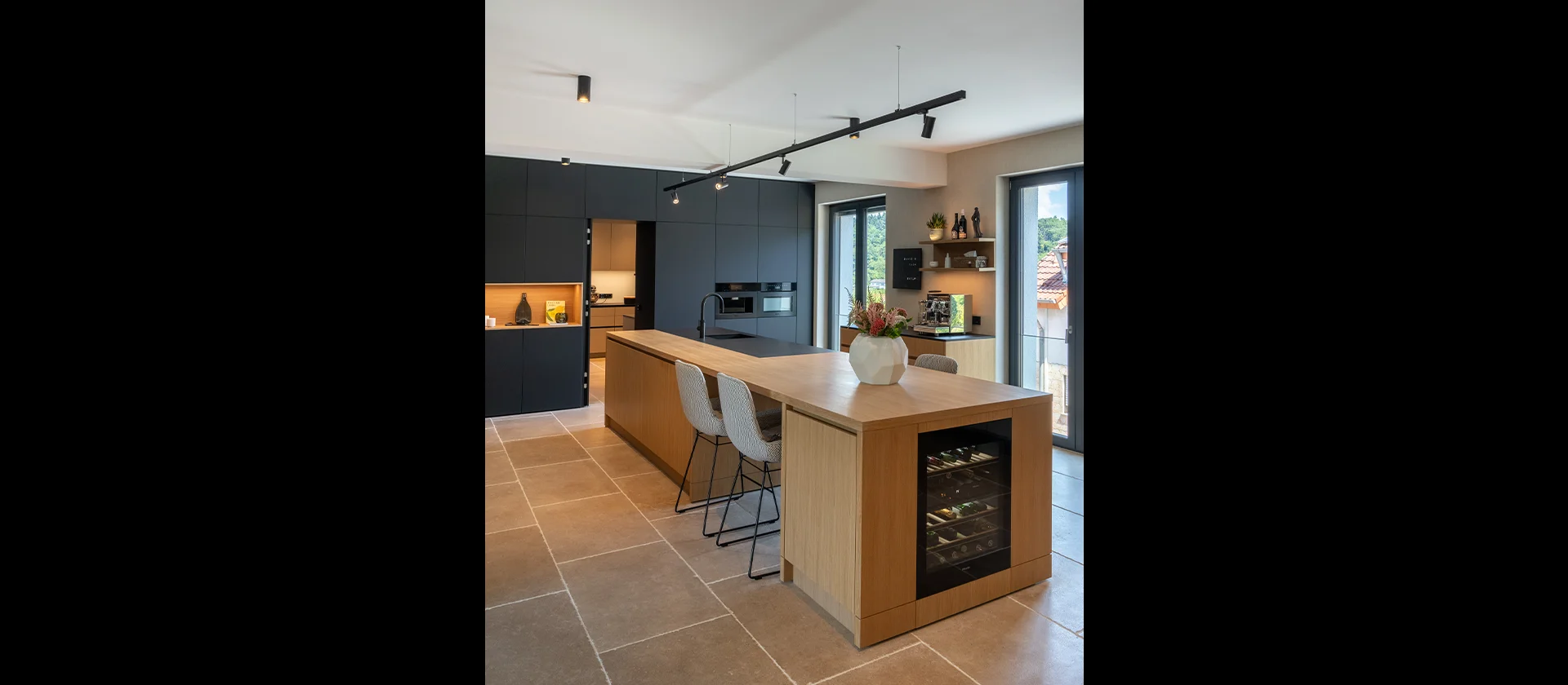 Designküche mit schwarzer Schrankfront, heller Holzinsel, Weinkühlschrank und Blumenvase als Dekoration