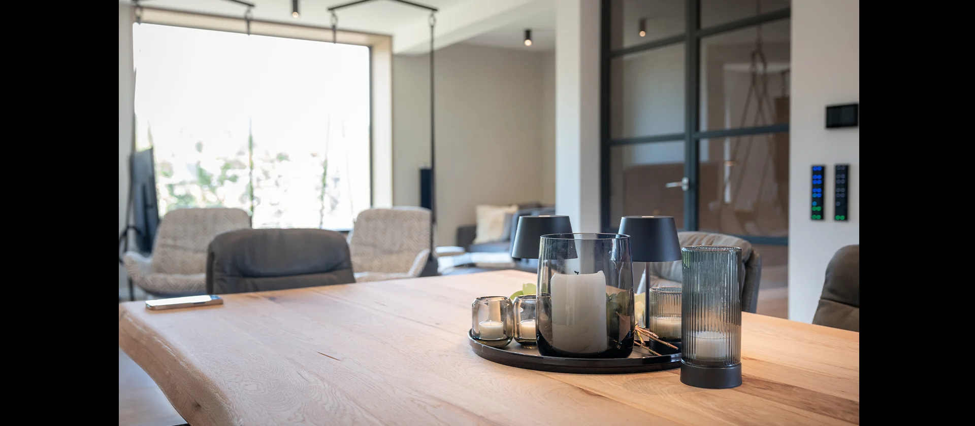 Detailaufnahme eines Esstisches aus massiver Eiche mit naturbelassener Baumkante, dekoriert mit Kerzen und Lampen, im Hintergrund Designküche in Fenix schwarz matt