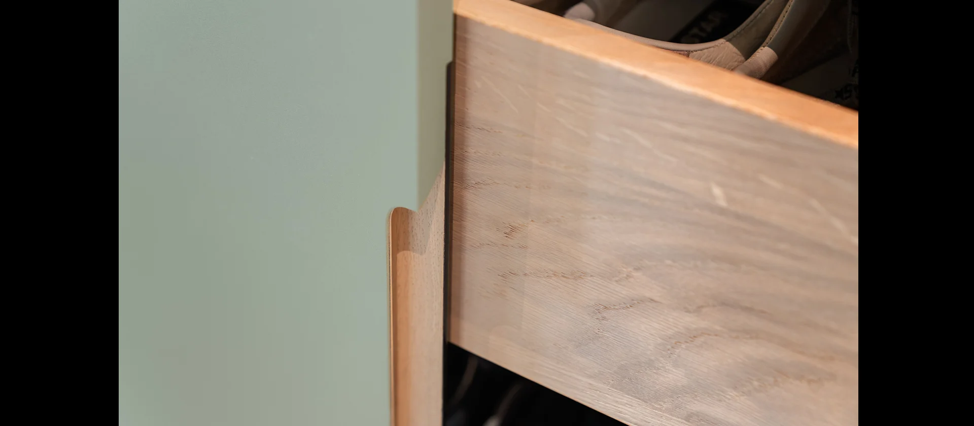 Detailaufnahme einer Schublade mit elegant gefrästem Griff in grün lackierter Oberfläche und massiver Front aus Eichenholz