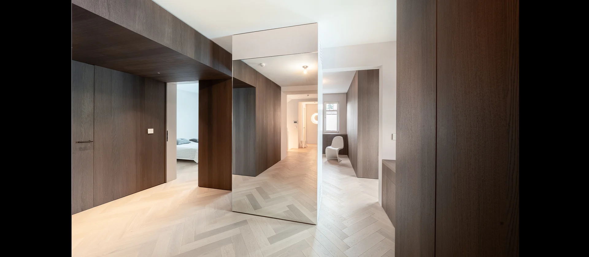 Flurbereich mit deckenhohen Wandverkleidungen in dunklem Holz, zentral platzierter Spiegelschrank erzeugt visuelle Tiefe und Raumwirkung