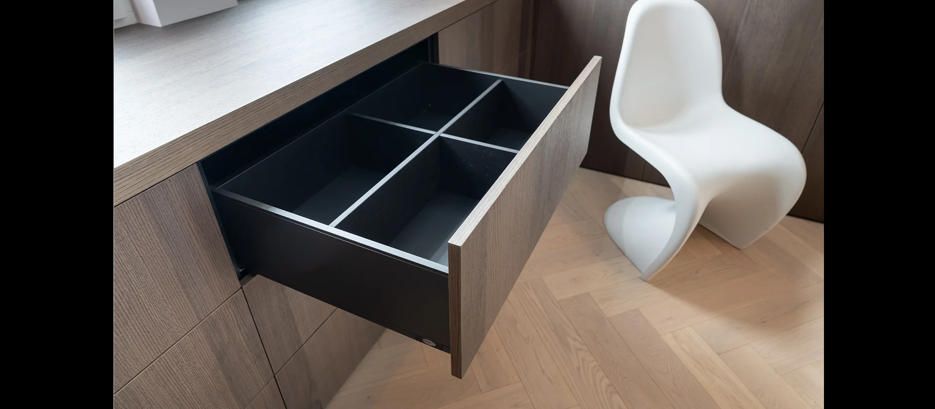 Geöffnete Schublade mit schwarzem Innenleben und vier Fächern, Teil einer maßgefertigten Holzkommode neben einem weißen Designstuhl