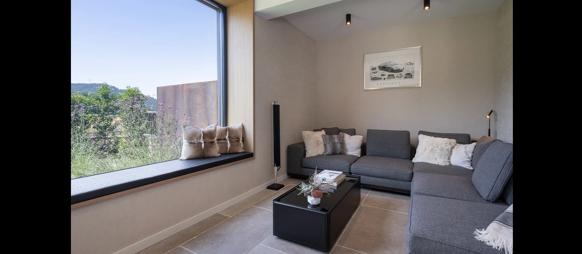 Moderne Sofaecke mit grauem Ecksofa, großem Fensterplatz mit Kissen und Couchtisch im gemütlichen Wohnbereich