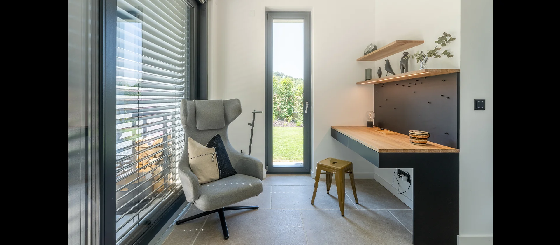 Stilvolle Arbeitsecke mit maßgefertigtem Holzschreibtisch, Wandregalen, Loungesessel und Blick ins Grüne durch hohe Fensterfront