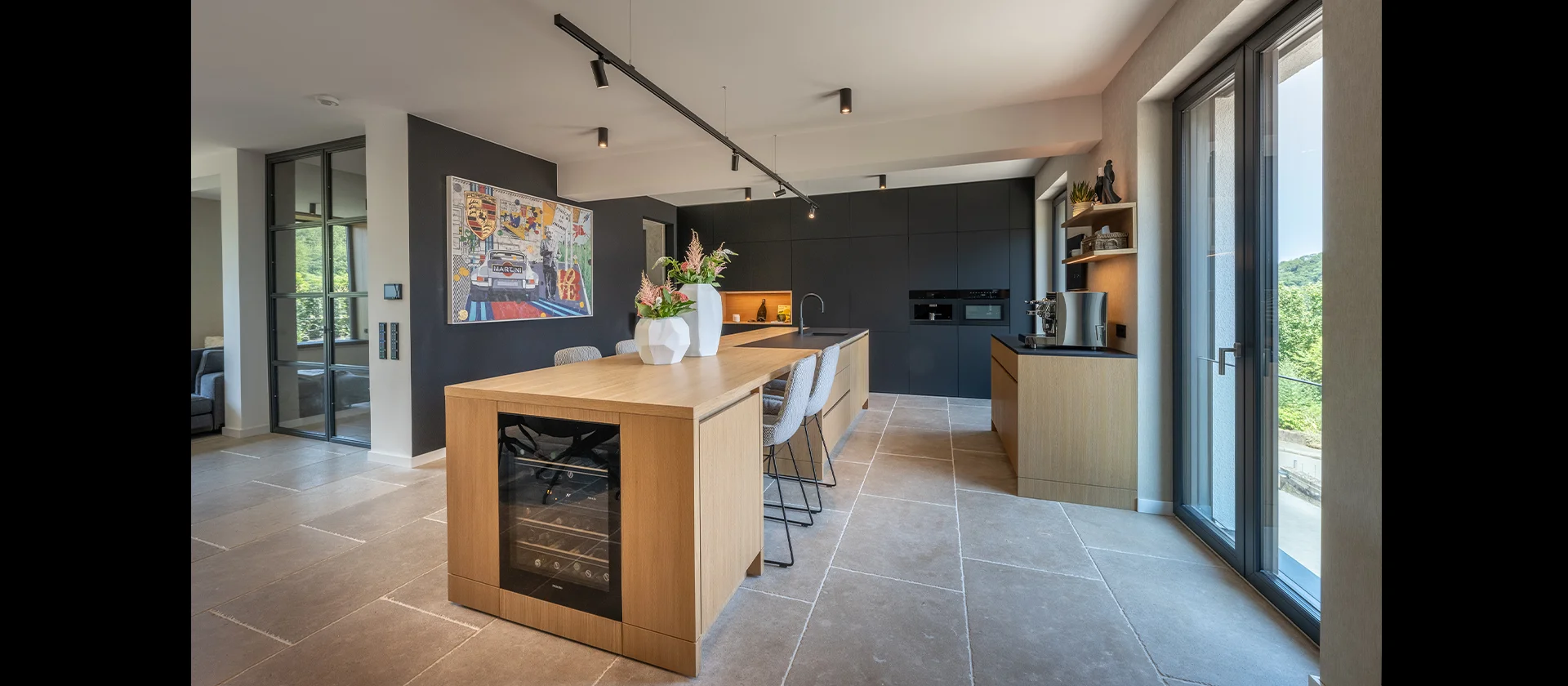 Offene Designküche mit Kochinsel, schwarzen Einbauschränken, Weinkühlschrank und Pop-Art-Bild an der Wand