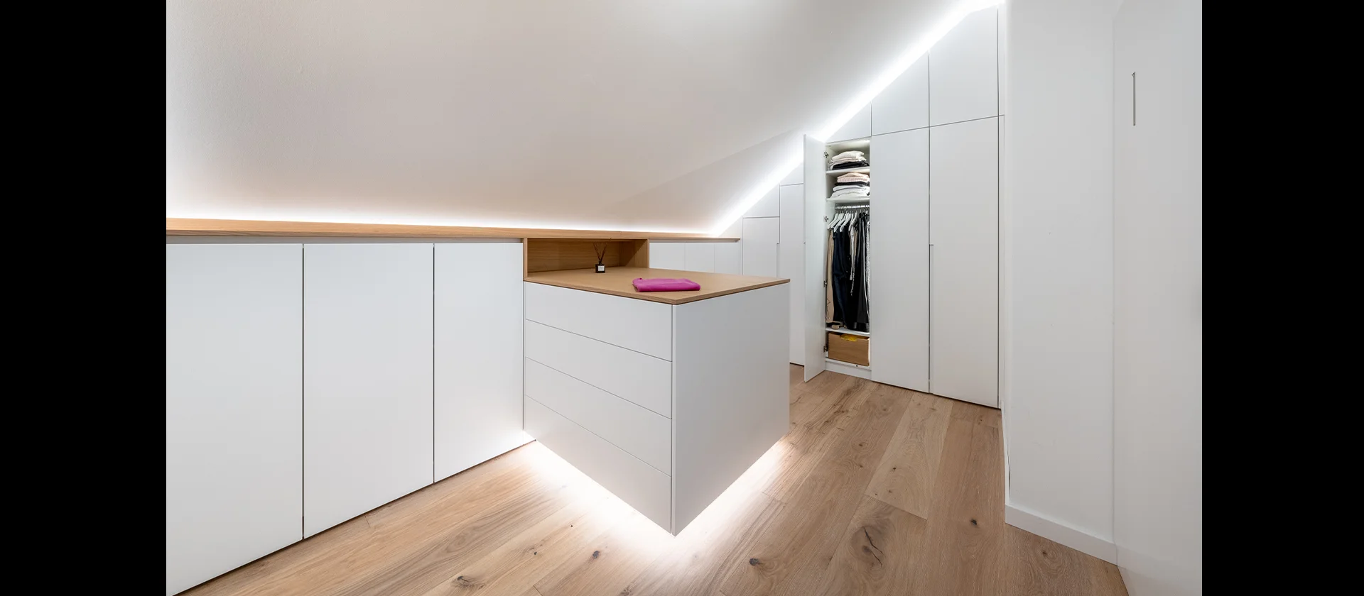 Weißer Einbauschrank unter Dachschräge mit geöffnetem Kleiderschrank und LED-Beleuchtung
